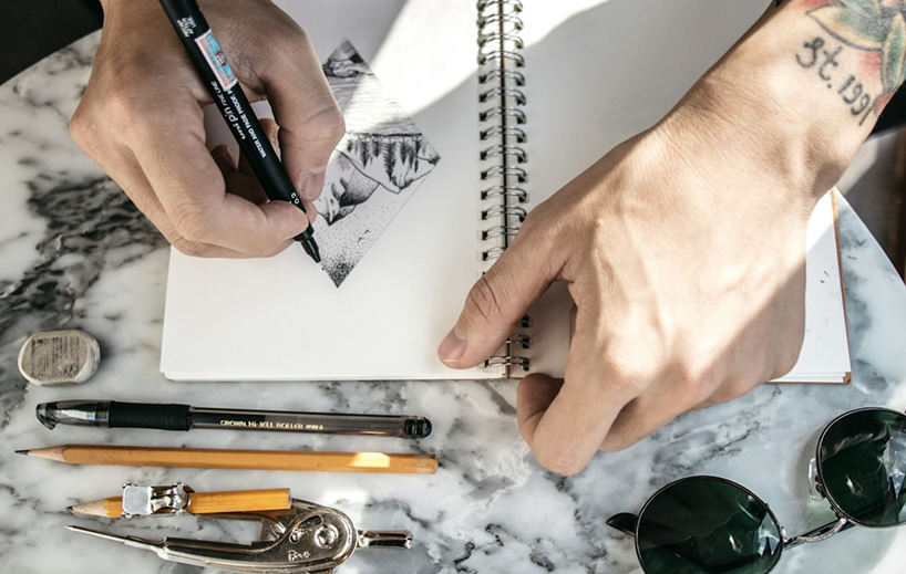 Hand sketching a tattoo design in a notebook